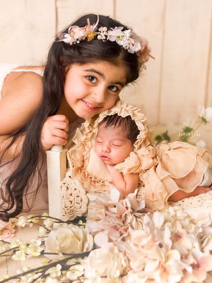 A big sister peeks over her sleeping newborn sibling with a curious and loving smile. It's a precious, authentic moment from a newborn photoshoot.