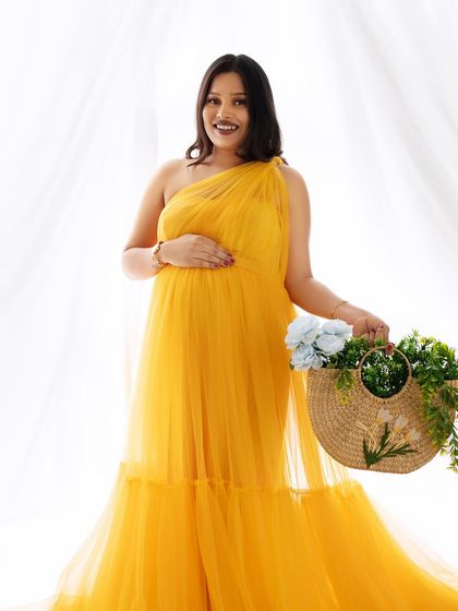 A bright and sunny portrait of a mom-to-be in a vibrant yellow one-shoulder gown, holding a basket of flowers.