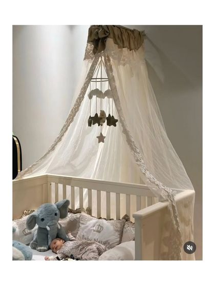 A full view of a serene and elegant nursery. The custom bedding with personalized pillows is perfectly complemented by a flowing lace canopy and a star and cloud mobile, creating a peaceful sleeping environment.