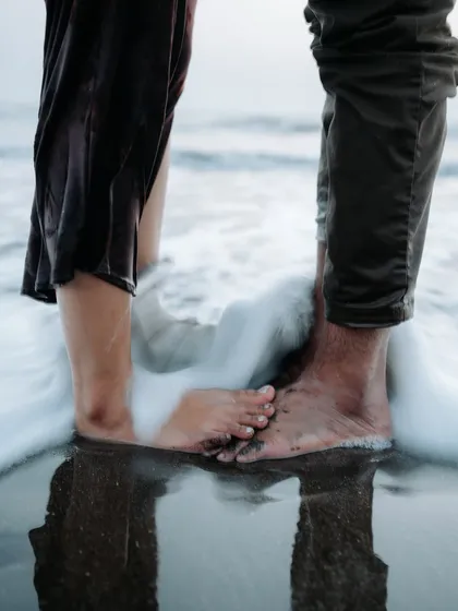 A creative close-up focusing on the couple's feet in the ocean surf, symbolizing their journey together. It's the small, artistic details that make a pre-wedding album special.