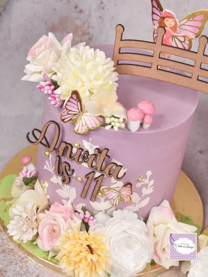 A close-up of one of the fairy garden cakes, adorned with flowers, butterflies, and a tiny fairy door.