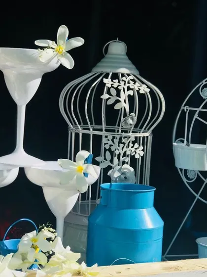 Whimsical white decor pieces that enhance the Santorini theme. This arrangement includes a decorative birdcage, a miniature Ferris wheel, and unique stacked margarita glasses, all in a clean white palette.