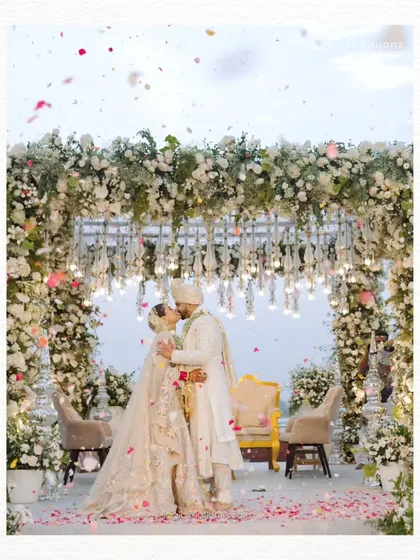 A perfect kiss under a canopy of white flowers. This mandap, set against the open sky, provided a stunningly romantic backdrop for the couple's first moments as husband and wife.