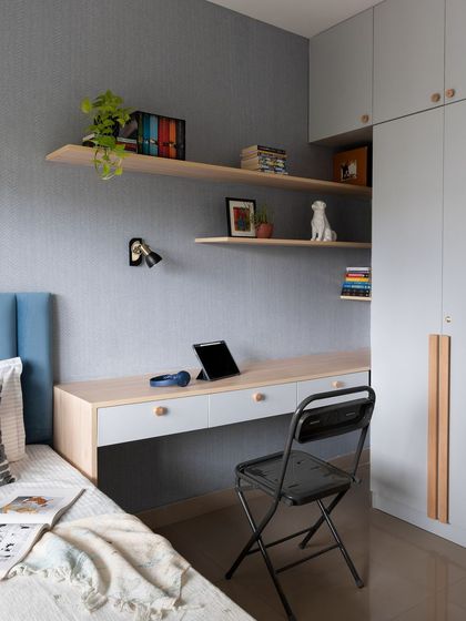This study area, integrated next to the bed, uses a cool grey and light wood palette. Floating shelves provide storage without taking up floor space, making it a perfect solution for a compact kid's room.