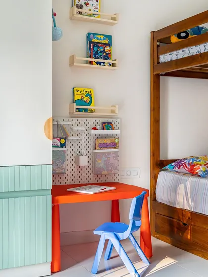 A close-up of the study area in the kids' room, with a bright red table and blue chair, and a pegboard organizer for art supplies.