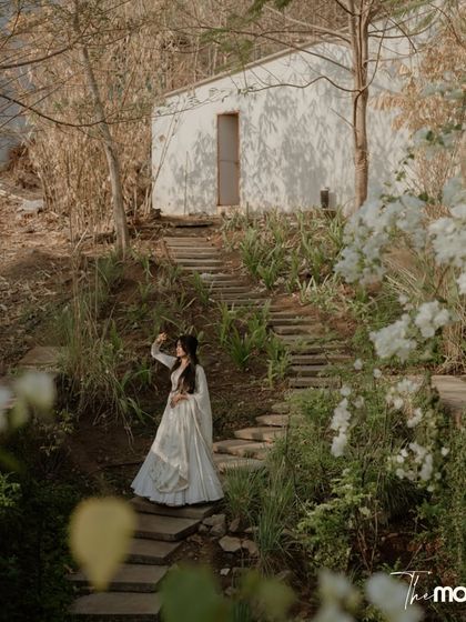 A solo shot of the bride during her pre-wedding shoot. She stands on a rustic stone path surrounded by nature, looking off into the distance, creating a sense of adventure and romance.