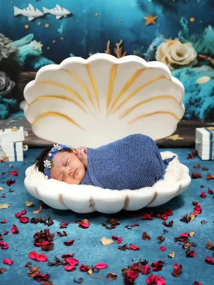 A pearl in the deep blue sea. This newborn is wrapped in blue and sleeping in a seashell, with an underwater backdrop creating a magical ocean scene.