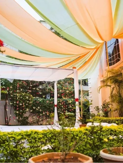 We transformed this home garden into a serene sanctuary for an intimate wedding ceremony. A simple white mandap is framed by flowing pastel drapes in mint green and soft peach, creating a dreamy canopy overhead. This design showcases our ability to create an elegant and romantic atmosphere using fabric and the natural beauty of your home's surroundings.