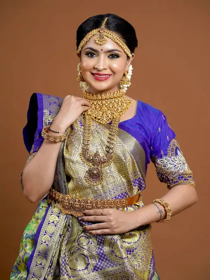 A beautiful bride in a blue and gold saree, wearing a full temple jewellery set.