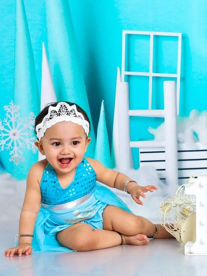 A happy princess in her winter wonderland. The "One" sign signifies a magical first birthday celebration in our Frozen-themed studio.