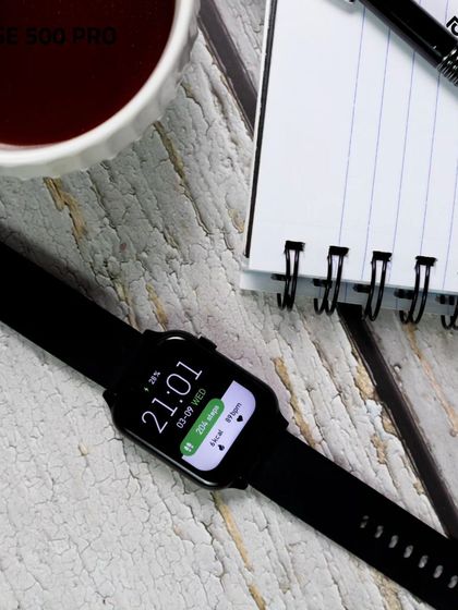 A flatlay of the smartwatch on a rustic wooden desk next to a cup of black coffee and a notepad. This composition creates a productive morning vibe, highlighting the watch as an essential daily tool.