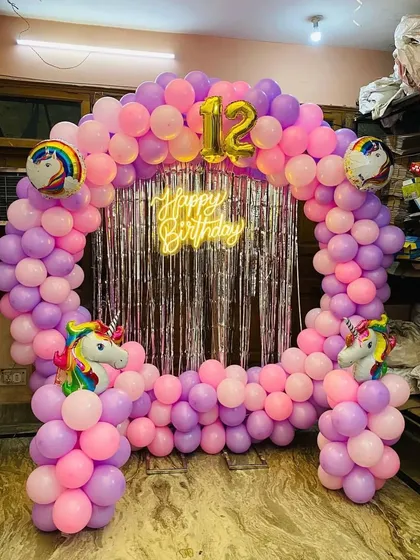 A magical unicorn-themed balloon arch for a 12th birthday, using pink and purple balloons, a silver fringe curtain, and unicorn foil balloons.