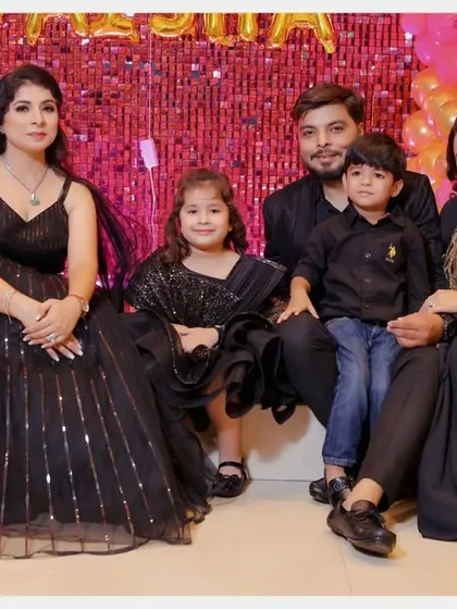 A formal family portrait from Taisha's birthday celebration. The family coordinated in elegant black outfits against a sparkling pink and gold backdrop, making for a stunning group photo.