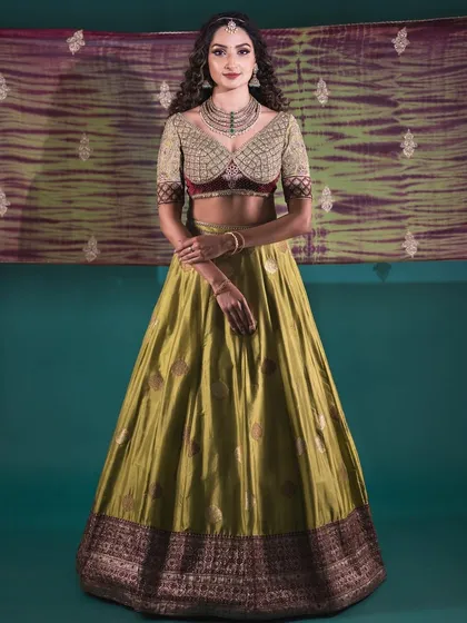 A full-length portrait of the model in the olive green Banarasi lehenga. The rich colors and flowing silhouette make it a stunning choice for a reception or sangeet.