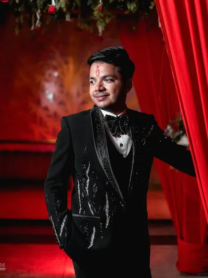 A close-up portrait of the groom against a vibrant red backdrop. His slight smile and confident pose make for a strong and stylish engagement photo.