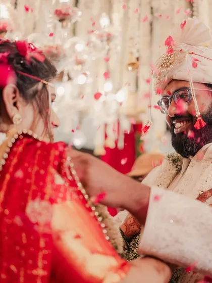 A candid shot capturing the laughter and joy during a traditional wedding ceremony. The air is filled with petals, and the couple's happiness is palpable.