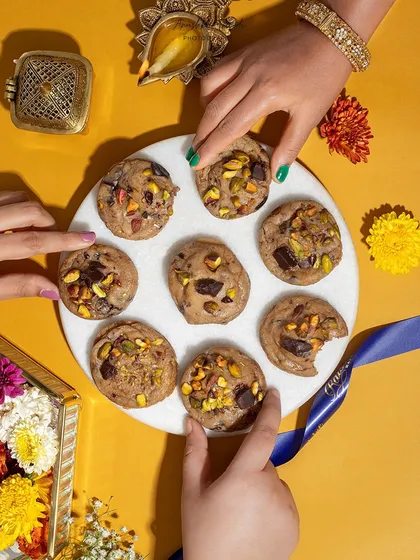 A top-down shot of multiple hands reaching for cookies on a platter. This image captures the fun and excitement of sharing treats during a festival like Diwali.