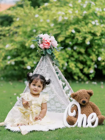 A sweet first birthday portrait of a little girl in a yellow dress, sitting in a teepee with her teddy bear.
