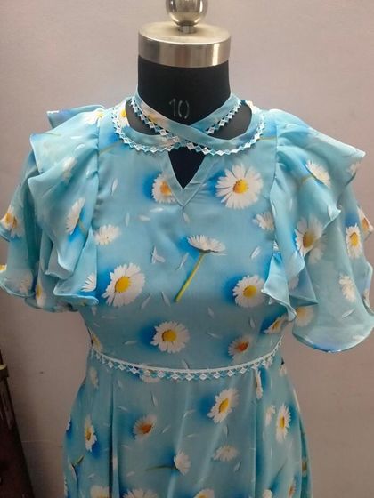 A lovely light blue summer dress with a daisy print. The design features a unique criss-cross neckline and layered ruffle sleeves for a playful, feminine look.