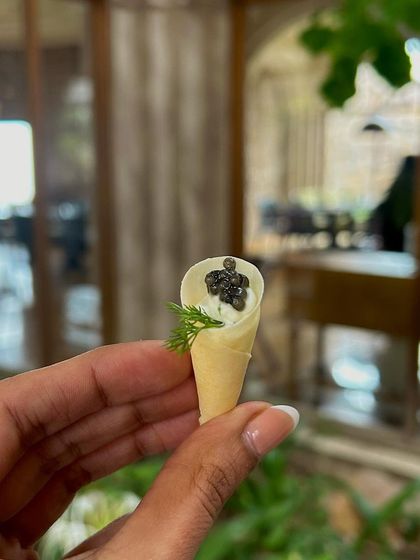 A hand holds up the delicate caviar cone, showcasing its small size and intricate preparation.