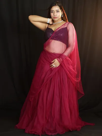 A full-length portrait against a black backdrop. The lighting from the side helps to define the model's silhouette and the flow of the lehenga.