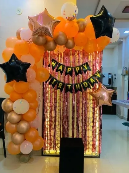 A simple yet stylish birthday photo corner. An orange, black, and rose gold balloon arch frames a shimmering fringe backdrop, perfect for taking party pictures.