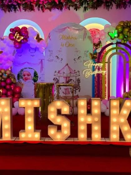 A whimsical carousel and butterfly theme for Mishka's first birthday. The grand stage setup features large light-up letters, a custom backdrop, and colorful balloon decorations.