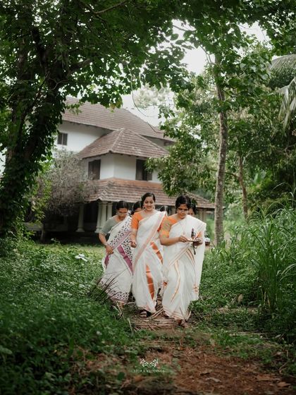 The bride and her family, all dressed in traditional Kerala sarees, walking towards a traditional tharavadu house.