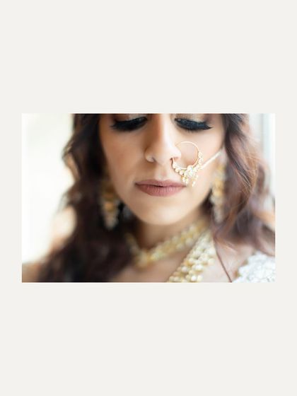 A close-up shot focusing on the bride's face and intricate nath. The soft focus and minimalist composition create a delicate and beautiful portrait.