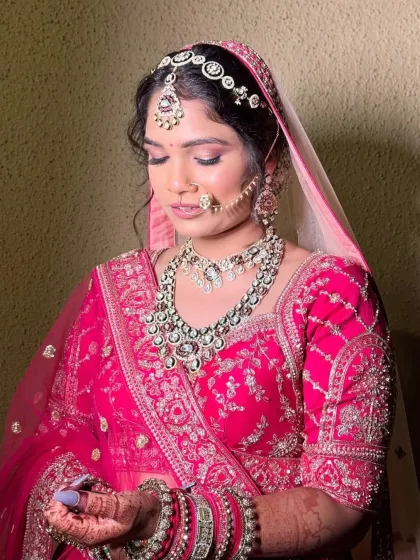 A close-up of a beautiful bride in her pink lehenga, looking down with a gentle smile. Her heavy kundan set, including the matha patti and nath, was the perfect choice for her grand celebration.