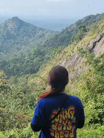 A traveler wearing a "Sunny Days Ahead" t-shirt looks out at the Edakkal Caves viewpoint in Wayanad.