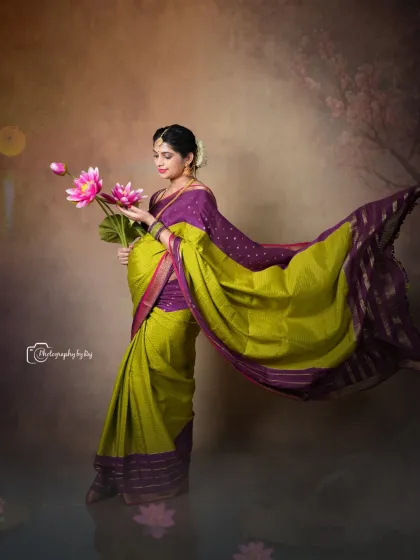 An artistic studio portrait of a mother-to-be in a traditional saree, holding lotus flowers. The flowing fabric and soft lighting create a dreamy effect.