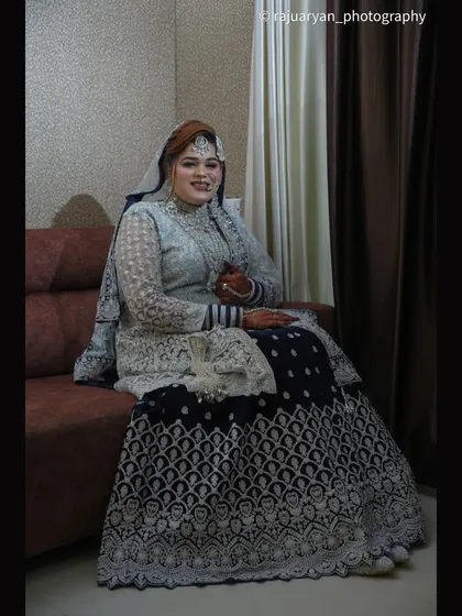 A relaxed and regal portrait of the bride seated. This pose allows her full lehenga to be displayed, showing the intricate patterns on the skirt.