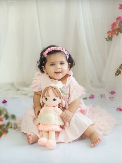 Best friends. This ten-month-old is posing with her favorite doll, both looking adorable in a pink-themed floral setting.