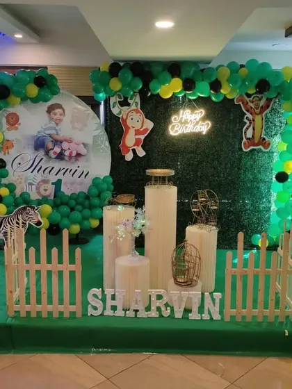 A personalized jungle theme featuring a photo of the birthday boy on a large circular backdrop, surrounded by green and black balloons and animal props.