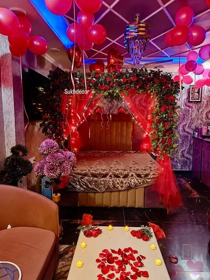 For a truly luxurious and nature-inspired look, I design setups with dense floral arrangements. This bed is framed by a stunning arch made of fresh red roses and lush greenery, combined with fairy lights and balloons to create a breathtaking floral canopy.