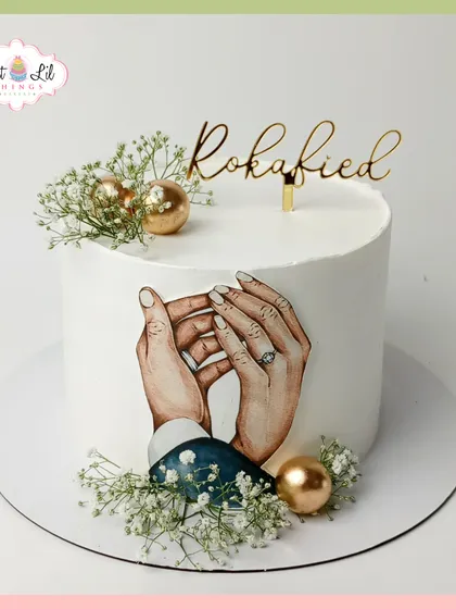"Rokafied!" This elegant engagement cake features a beautifully hand-painted image of holding hands, accented with delicate baby's breath and gold spheres.