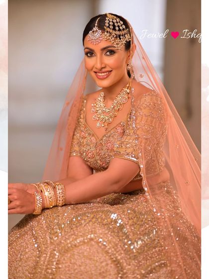 A full-length portrait of the bride seated, looking absolutely regal in her complete golden ensemble and uncut Polki jewellery.