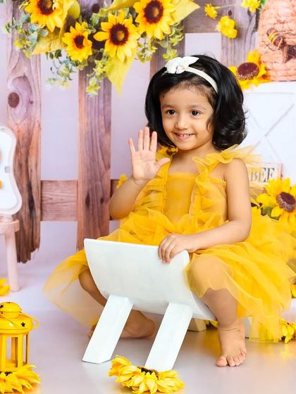 A sunny second birthday. This little girl, dressed in yellow, waves hello from our cheerful sunflower-themed set.