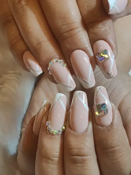 Elegance is in the details. This set of almond-shaped nail extensions features a neutral pink base with crisp white and silver line art. The look is elevated with a full accent nail of iridescent gems and a delicate crystal border on the pinky finger.