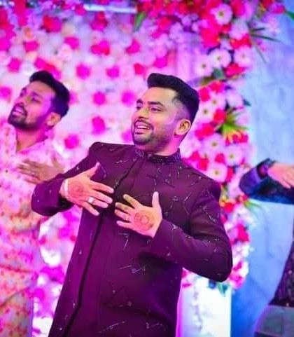 A groom enjoying his Sangeet performance in a wine-colored Indo-Western jacket. The abstract katdana work catches the light as he moves, making it perfect for a night of celebration.