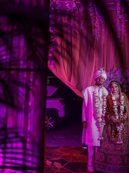 The couple stands together after their ceremony, framed by dramatic purple lighting and shadows. This artistic shot creates a modern and stylish wedding portrait.