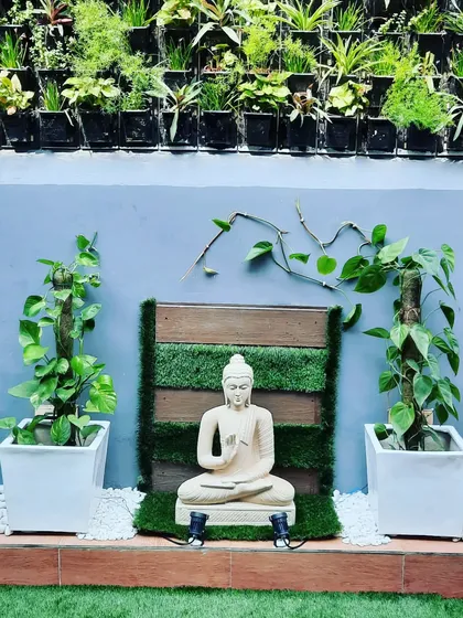 A close-up of the serene Buddha statue set against a wood and grass backdrop, with a full vertical garden above.