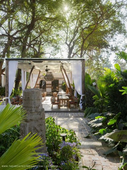 A view down a garden path at Sanctuary Bar towards an open-air dining pavilion. The lush planting and dappled sunlight create an enchanting and immersive experience for guests.