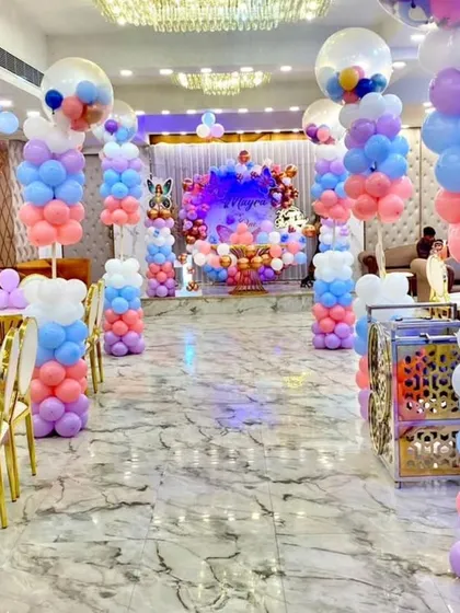 A whimsical butterfly themed birthday party filling a large hall. The aisle is lined with colorful pastel balloon pillars, leading to a stunning stage setup and creating a magical entrance for the guests.
