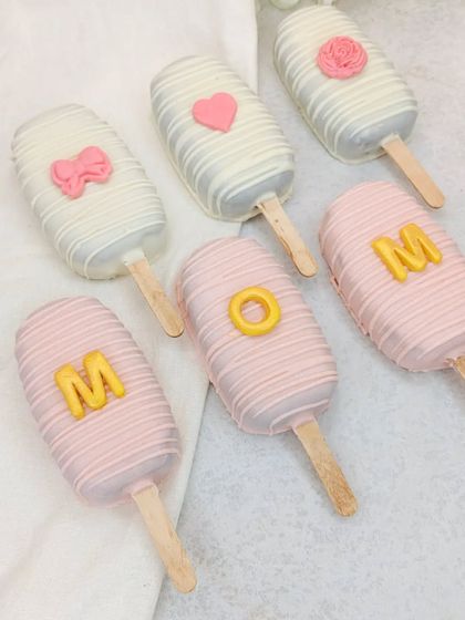 Our "MOM" cakesicles, decorated in pink and white chocolate, are a cute and delicious part of our Mother's Day hamper.