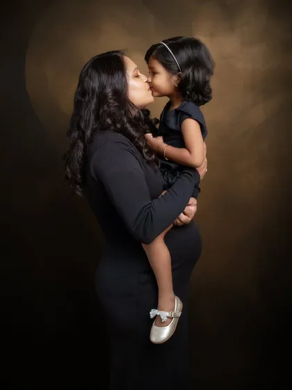 A tender kiss from a soon-to-be big sister. This classic, dark-toned portrait focuses on the intimate connection between mother and child, creating a timeless and emotional piece of art.