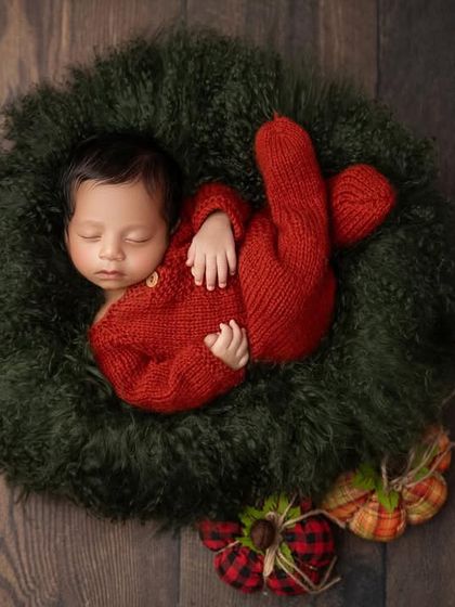 An overhead view of the newborn in a Christmas wreath, showcasing the rich textures of the dark wood floor and the soft, fluffy wreath, making the baby the star of the show.
