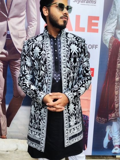 A client wearing a black open sherwani with heavy white embroidery, layered over a black kurta. This is a bold, high-contrast look perfect for making an impression.