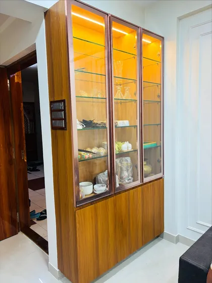 A custom-built crockery unit designed with a wooden base and glass display cabinets. The rose-gold metal frame and internal backlighting provide an elegant way to store and showcase fine dinnerware.